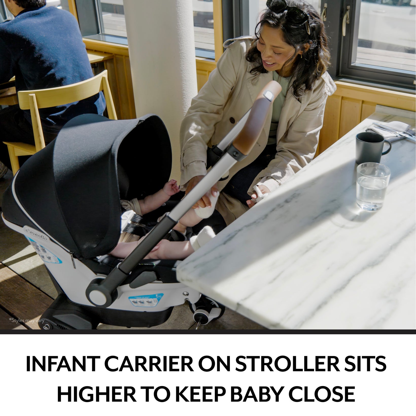 A woman smiles at a baby in a white and black Evenflo car seat, which is converted into a stroller, at a cafe table.