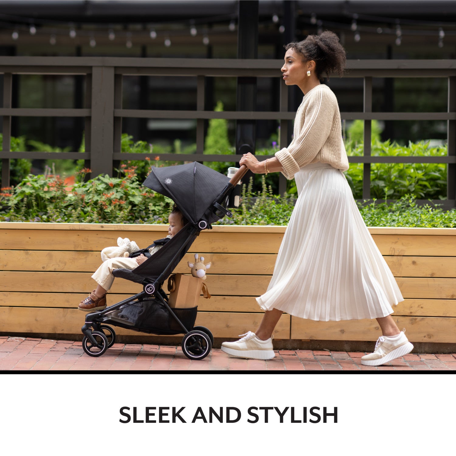 A fashionable mother walks confidently, pushing her happy baby in a sleek, black stroller.