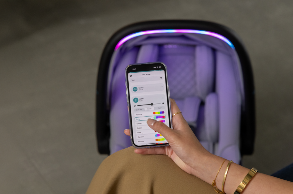 A person's hand using a phone app to change the color of a light strip on a purple car seat.