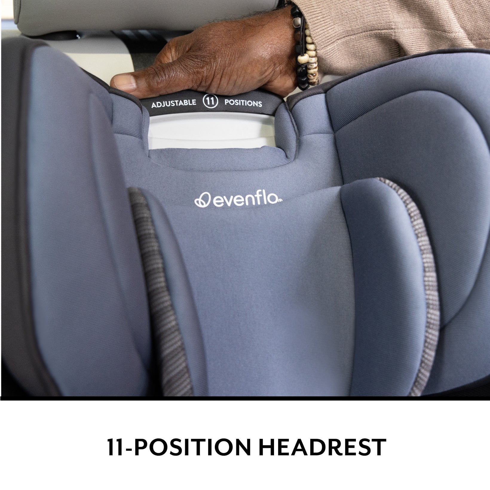 A hand adjusts the eleven-position headrest on a gray Evenflo car seat, with the brand logo visible.