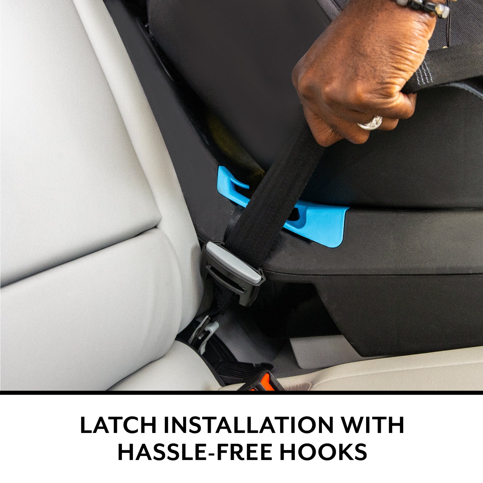 A person's hand adjusts a car seat belt through a blue guide on a black booster seat.