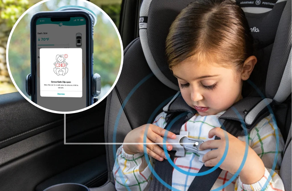 A child in a car seat with a safety sensor clip on the chest strap, and a phone screen