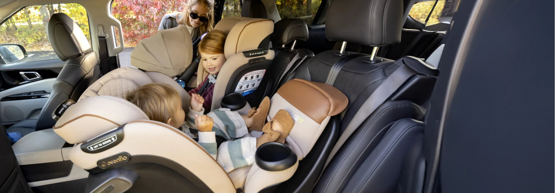 Two young children sitting in car seats in the back of a car, with an adult partially visible.