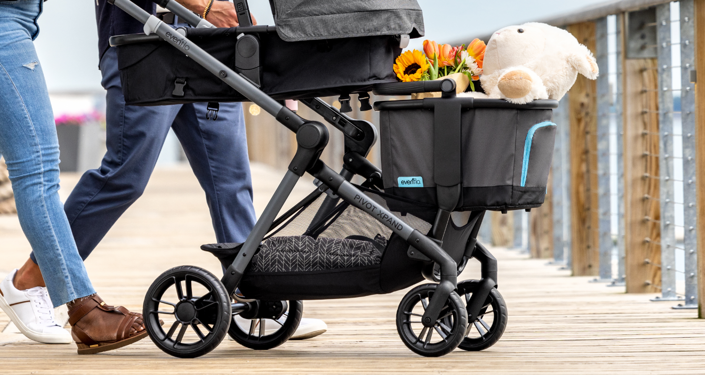 Person pushing a stroller with a child inside, on a wooden deck.