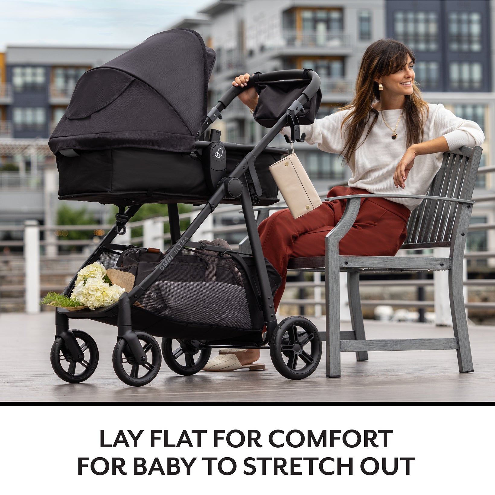 Woman sitting on a chair next to a black stroller with a baby in it, in an urban setting.