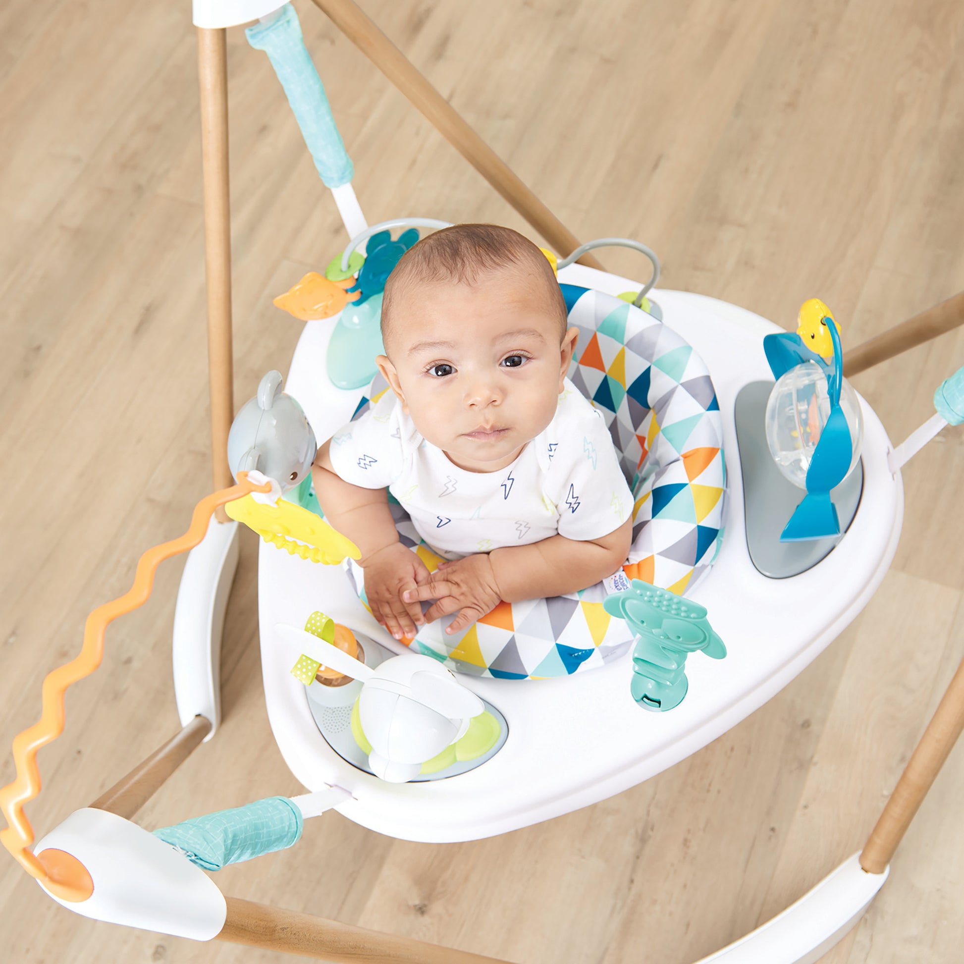 Baby with a serious face playing in a bouncer activity center with a geometric pattern.