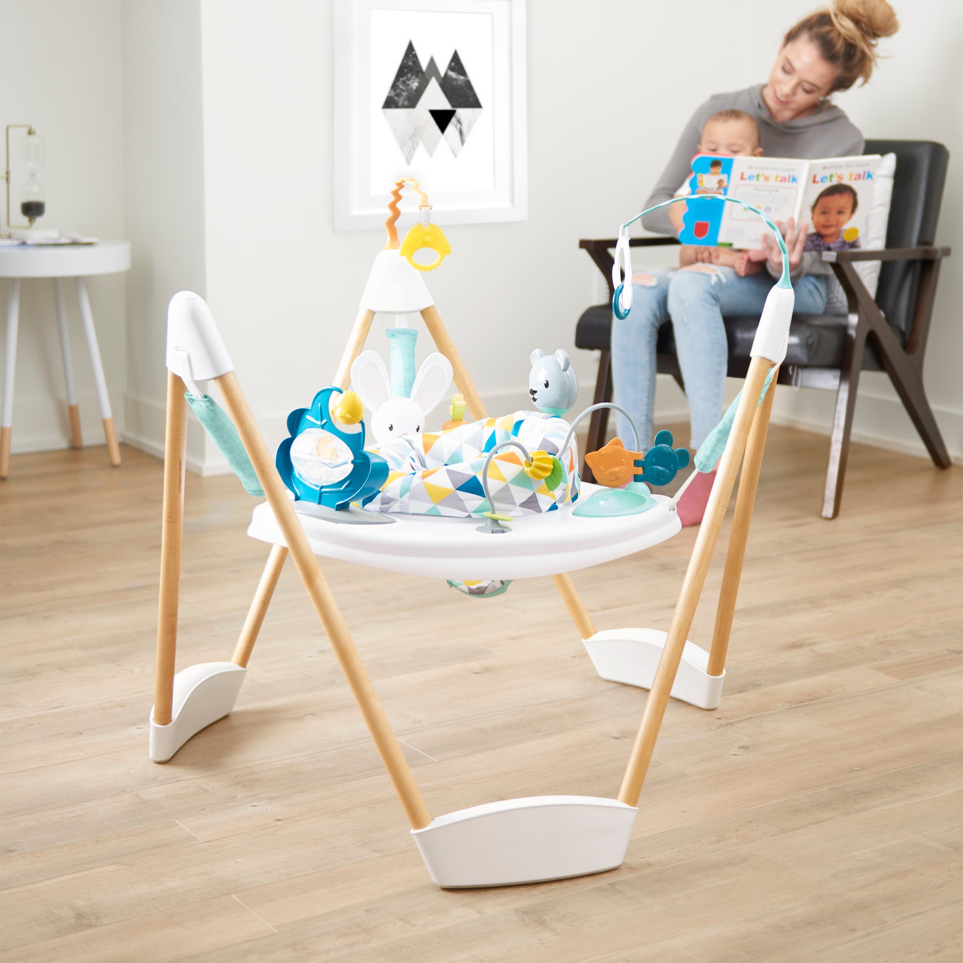 Woman reading to a baby while another baby plays in the bouncer activity center.