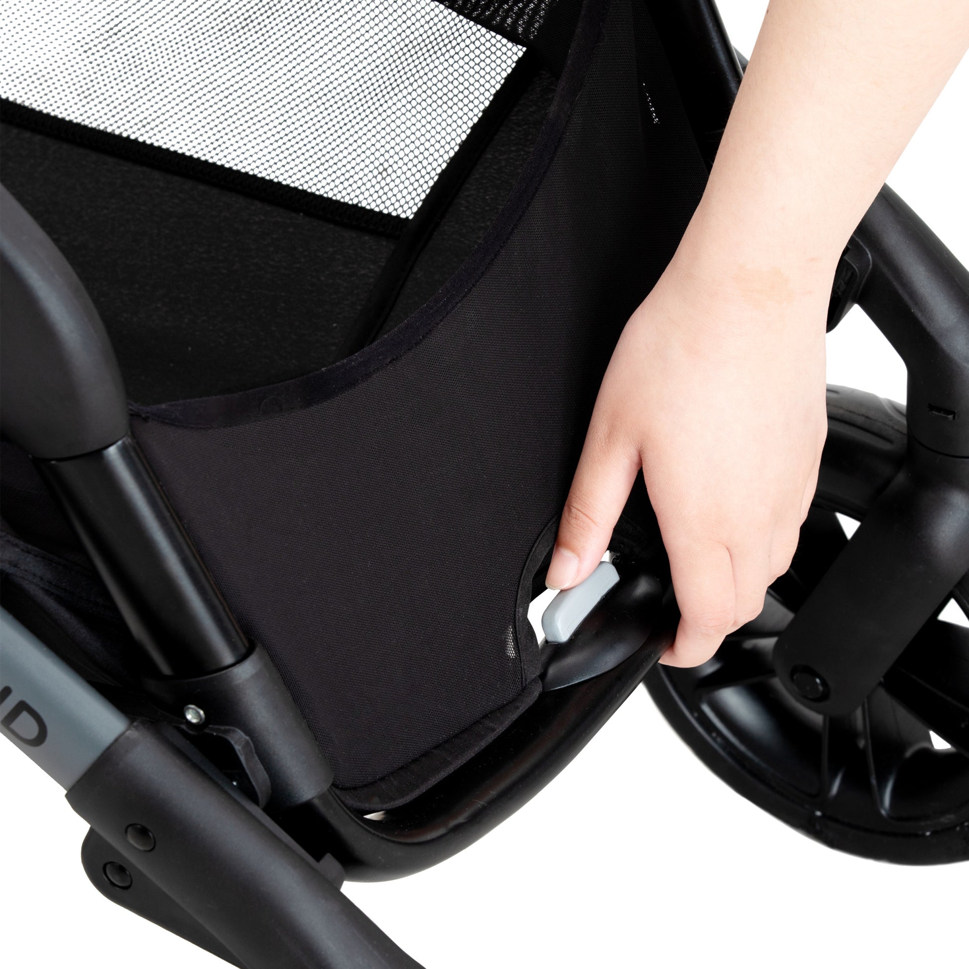 A hand pressing a gray button on a stroller, likely for folding or adjusting the seat.