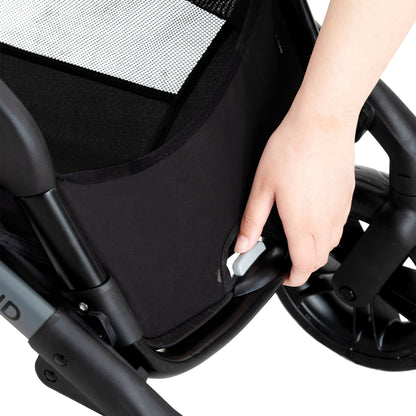 A hand pressing a gray button on a stroller, likely for folding or adjusting the seat.