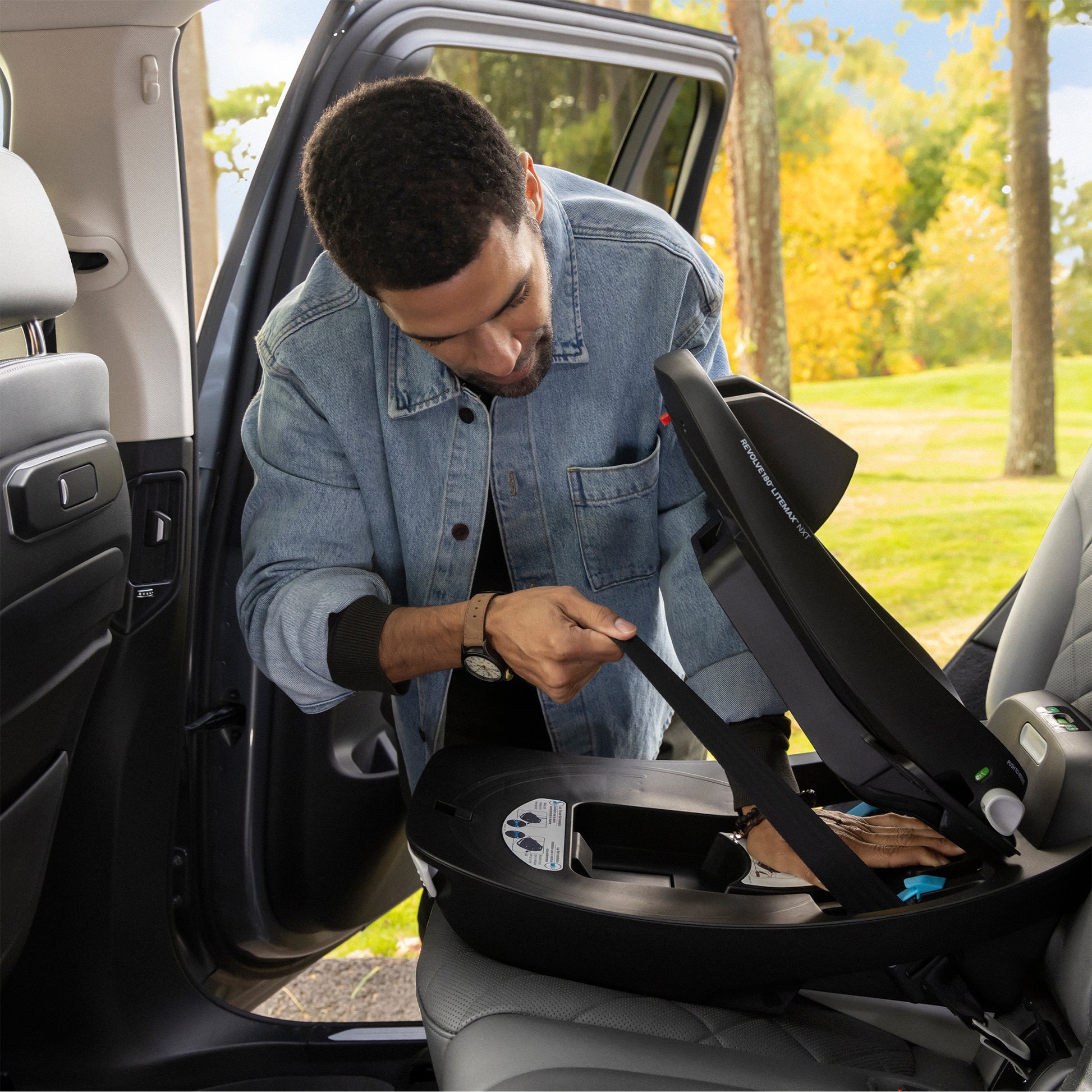 Man adjusting a car seat in a vehicle with a scenic outdoor background