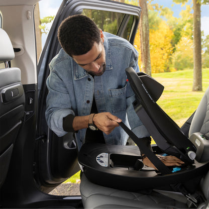 Man adjusting a car seat in a vehicle with a scenic outdoor background