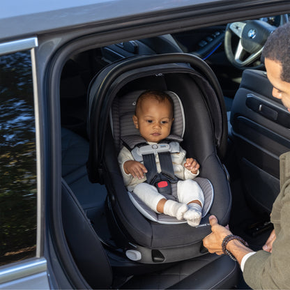 Baby in a car seat being secured by an adult in a vehicle.
